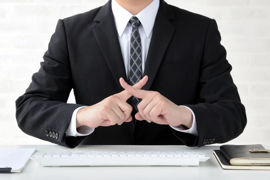 スーツをきた男性が✕を指で作っている