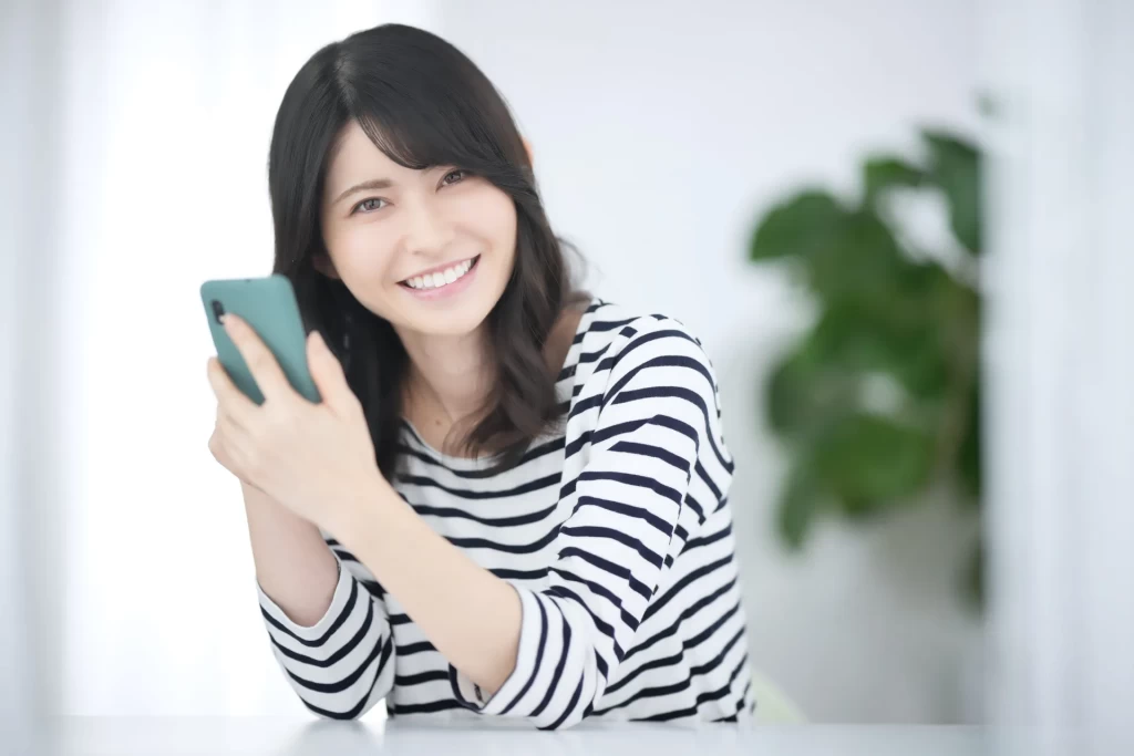 スマホをもってこちらを笑顔で見ている女性