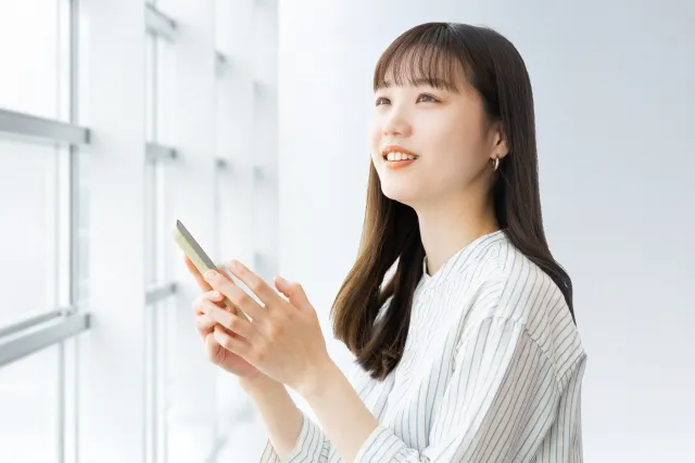 窓際でスマホをもち外を見ている女性