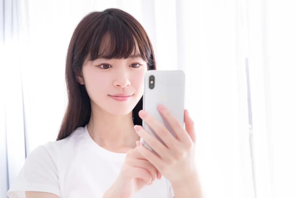 ほほえみながらスマホを操作するロングヘアの女性