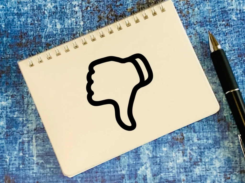 親指を下にするマーク(サムズダウン)が表示されたノートとペン