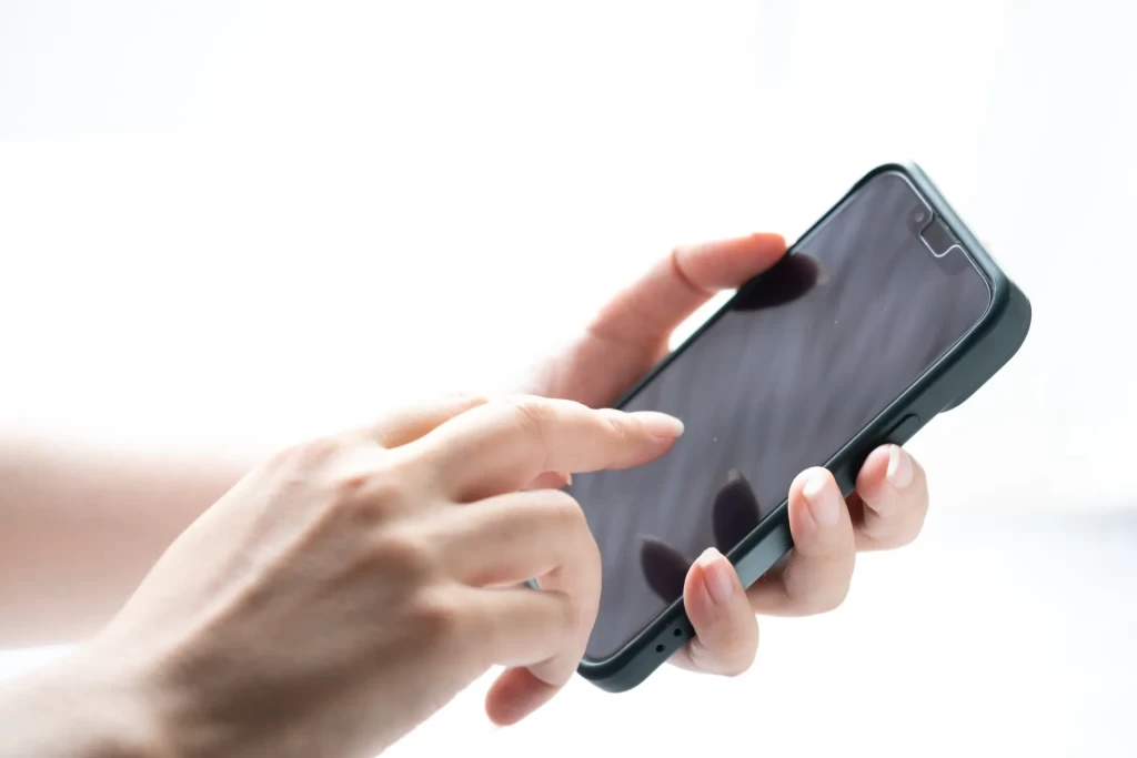 左手にスマホを持って、右手で操作しようとしている女性の手元