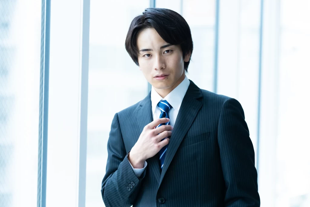 ネクタイに右手をかけて真剣な表情を見せるスーツ姿の男性