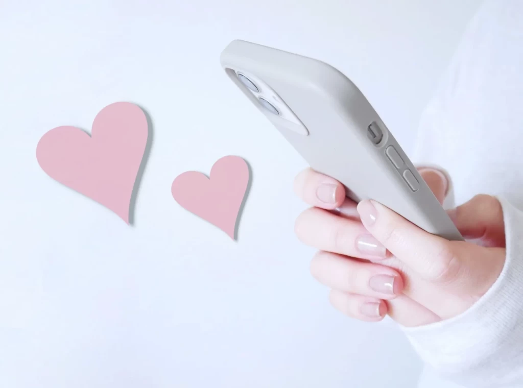 両手でスマホを包み込むように持つ女性の手元と、2つ並んだハートマーク